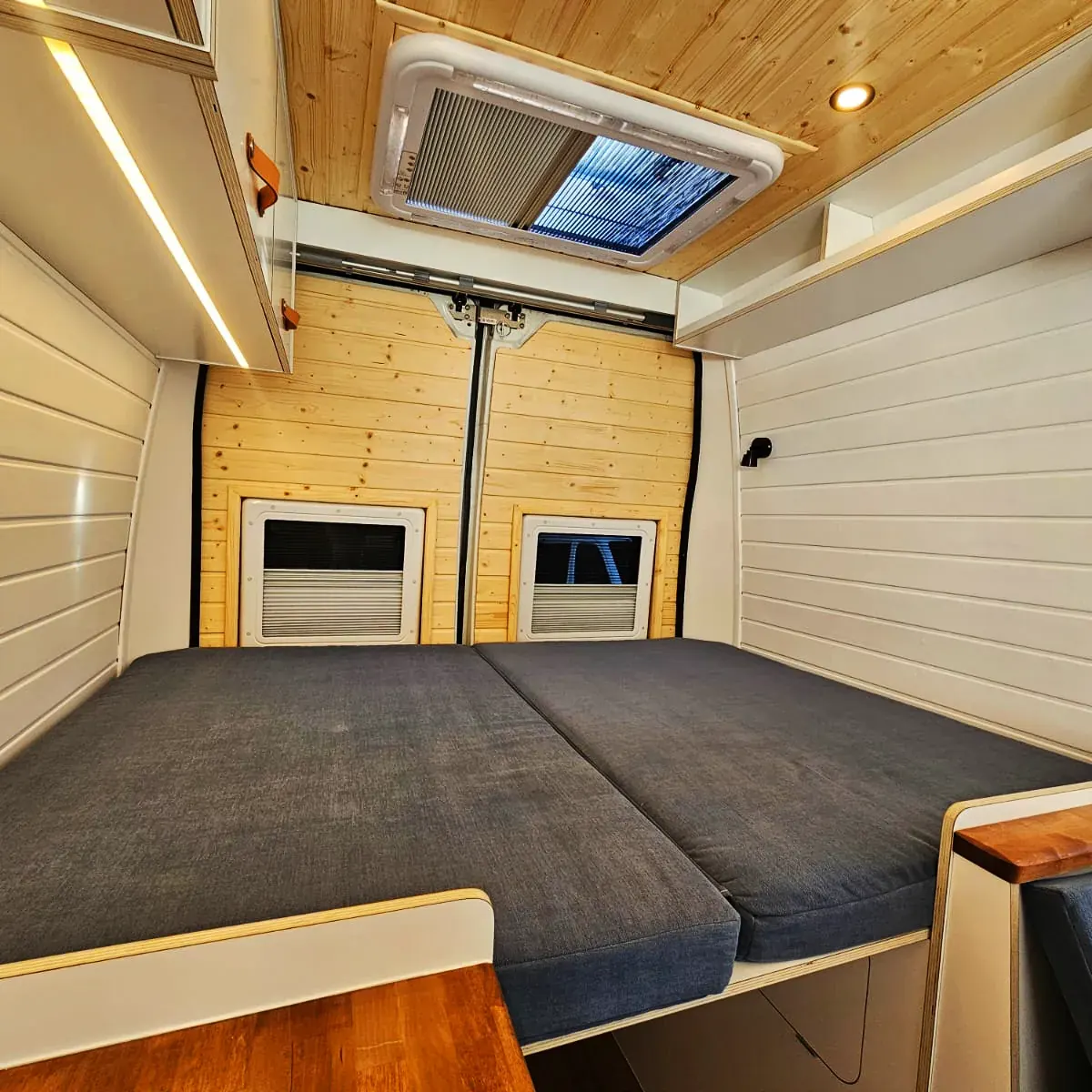 Cama transversal de matrimonio en una camper con claraboya