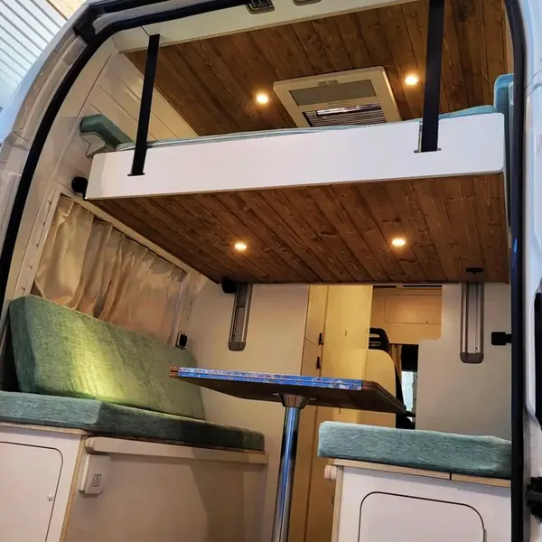 Cama elevable sobre la dinette de una camper con techo de madera
