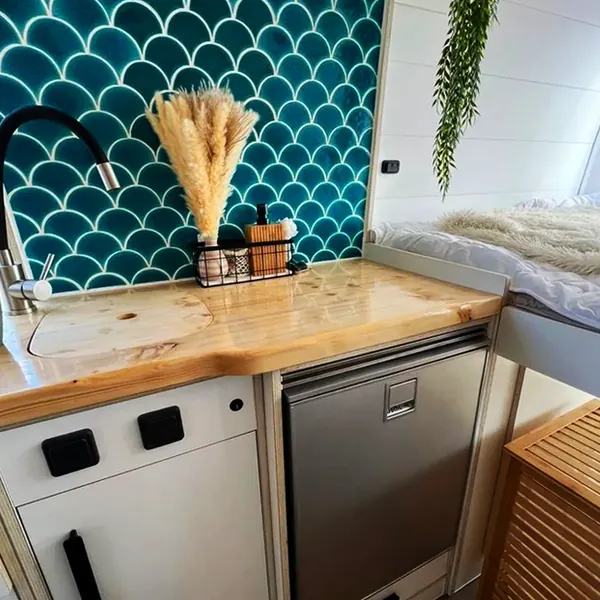 Cocina de camper con azulejo de escamas verde, encimera de madera y nevera