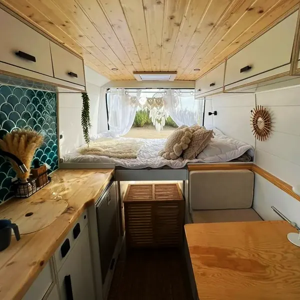 Interior de camper con cama trasera, cocina con azulejo verde y techo de madera